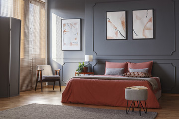 gray, retro armchair standing in the corner of an elegant bedroom interior with watercolor posters o