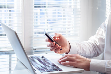 Businessman working with laptop and smartphone, bright office, financial accountant