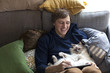 © Ulrika Kestere - Young man sitting with iPad in sofa with cat sleeping on his belly