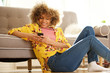 © mimagephotos - attractive african american woman sitting on floor at home and using mobile phone