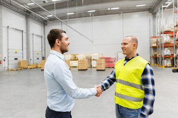 logistic business and cooperation concept - manual worker and businessman with clipboard shaking hands and making deal at warehouse