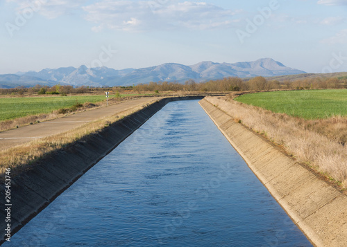 Fotomural Canal de agua para el riego en paisaje con montañas al fondo