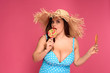 © LIGHTFIELD STUDIOS - beautiful size plus model in swimsuit holding lollipops and looking at camera isolated on pink