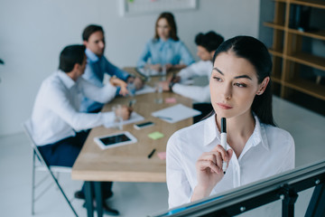 selective focus of pensive businesswoman and colleagues behind at workplace in office