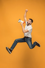 Jumping Fan On Orange Background. The Young Man As Soccer Football Fan With Megaphone