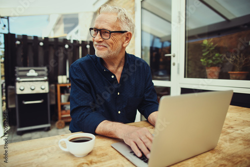 Foto Smiling senior man drinking coffee and using a laptop