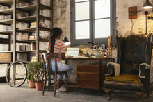 Back View Of Young Woman Sitting At Desk In A Loft Working On Laptop