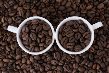 Two white cups with coffee beans on the background of coffee beans