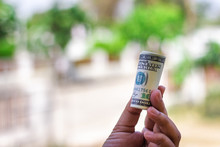 A Man's Hand Holding A Rolled Up Banknote Used For Payments Illustrates Currency Exchange Investments And Savings That Result In Economies Success That Make People's Money..Financial Concepts
