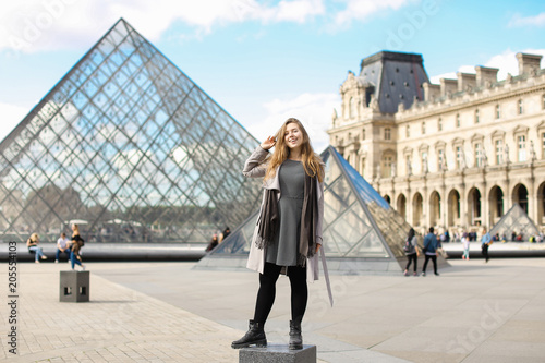 Photographie Girl wearing grey coat and standing near Louvre and glass pyramid
