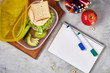 Concept of school lunch break with healthy lunch box and school supplies on white desk, selective focus, flat lay