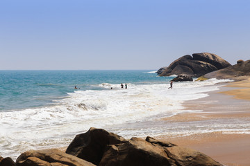 Wall Mural - group of people swimming on a large sandy beach with big rocks