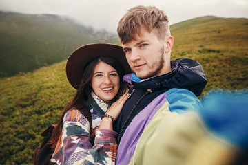 Wall Mural - happy hipster couple making selfie on top of sunny mountains. summer vacation. space for text. atmospheric moment. travel and wanderlust concept. stylish man and woman traveling.