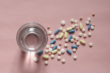Overhead View Of Medicines With Drinking Water In Glass Over Coral Background