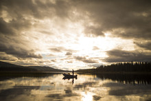 Distant View Of Father And Son In Boat On Lake Against Cloudy Sky During Sunset