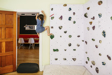 Full Length Of Girl Practicing On Climbing Wall In Bedroom At Home