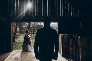 Wall Mural - stylish groom walking to his beautiful bride in sun light in wooden barn. rustic wedding concept, space for text. happy bohemian newlyweds . modern couple