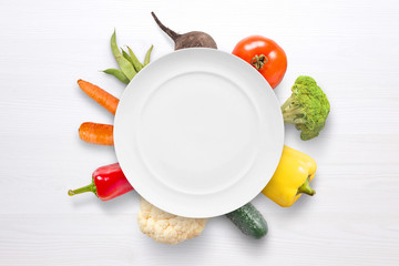 Empty plate with vegetables in background on white wooden surface.