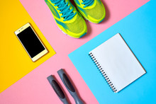 Sports Equipment With Shoes, Skipping Rope, Blank Notebook And Mobile Cellphone With Earphones On Colorful Background. Top View, Flat Lay. Sport, Fitness Concept, Healthy Lifestyle