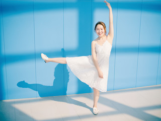 Wall Mural - Beautiful Chinese brunette woman in white wedding dress dancing and smiling at camera against blue wall background. Sunny portrait of glamour young stylish lady. Emotions, beauty and lifestyle concept