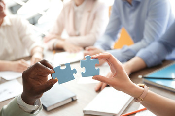 People with puzzle indoors, closeup of hands. Unity concept