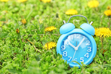 Poster - Alarm clock on green grass, outdoors. Time change concept