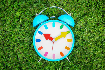 Poster - Alarm clock on green plants, outdoors. Time change concept