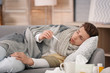 © New Africa - Sick young man with thermometer suffering from cold on sofa at home