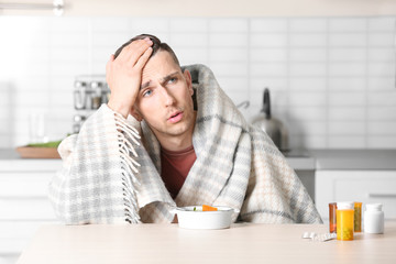 Poster - Sick young man eating broth to cure cold at table in kitchen