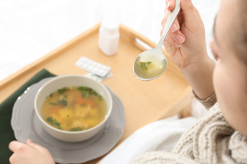 Poster - Sick young woman eating broth to cure cold in bed, closeup