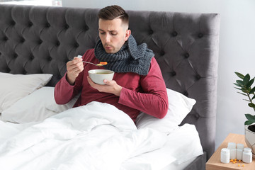 Poster - Sick young man eating broth to cure cold in bed at home