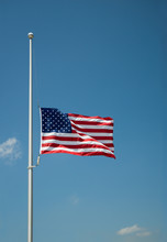 The United States Flag Flying At Half-mast Or Half-staff On A Flagpole. Blue Sky Background With Copy Space.