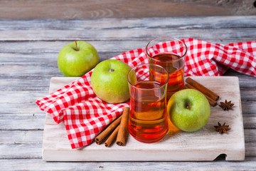 Wall Mural - Apple juice in glasses, spices and apples on wooden cutting table 