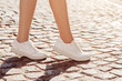 Fashion details: close up photo of woman's legs wearing trendy white leather sneakers. Model walking in street with paving stone. Natural sunny day light. Copy, empty space for text