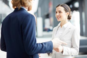 Sticker - Young businesswoman in suit listening to explanations of her colleague during their conversation in airport