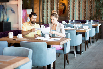 Wall Mural - Two young financiers sitting in cafe, reading financial documents and discussing them