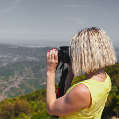 Wall Mural - Female traveler enjoying the views from the mountains of Montserrat in Spain and makes a photo on her camera. The girl in a yellow dress on background of the nature