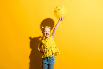 Girl with red hair on a yellow background. The girl touched up her hand in which the yellow balloon.