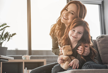 Portrait of delighted family sitting together in cuddles on sofa. They are looking at camera with big-toothed smile. Copy space in left side