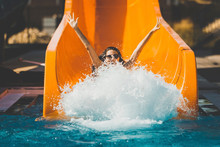 Joyful Woman Going Down On The Rubber Ring By The Orange Slide Make The Water Splashing In The Aqua Park. Summer Vacation. Weekend On Resort