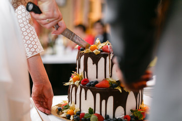 Wall Mural - Wedding cake with berries on wooden table. Bride and groom cut sweet cake on banquet in restaurant.
