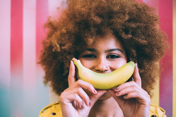 Surprised mixed race woman in a colorful artwork background wall playing with a banana