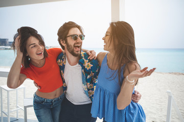 Lets life only in this moment. Portrait of joyful young man is embracing two women and laughing. They are standing at the beach 