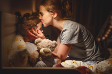 Mother Puts Her Daughter To Bed And Kisses Her In   Evening