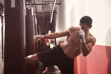 Canvas Print - Male kickboxer training with punching bag in gym