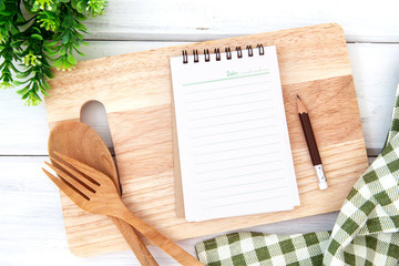 Sticker -  lined book notepad paper on chopping cutting board and tablecloth with wooden fork and spoon on white table , recipes food  for a healthy habits shot note background concept