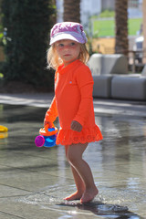 Very Cute Toddler, 2 Years Old Girl In Hot Orange Swimming Shirt, with  Blonde Hair and Big Blue Eyes, Playing outside in Hot Summer Day with Beach Toys and water, in Downtown Scottsdale Arizona USA