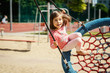 beautiful little girl is swinging on a swing at the playground on a summer day