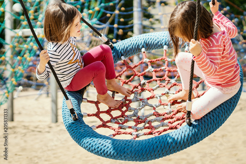 Fotografia two little girls are swinging on a swing at the playground on a summer day