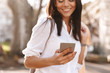 © Drobot Dean - Cropped image of Cheerful brunette woman in shirt using smartphone